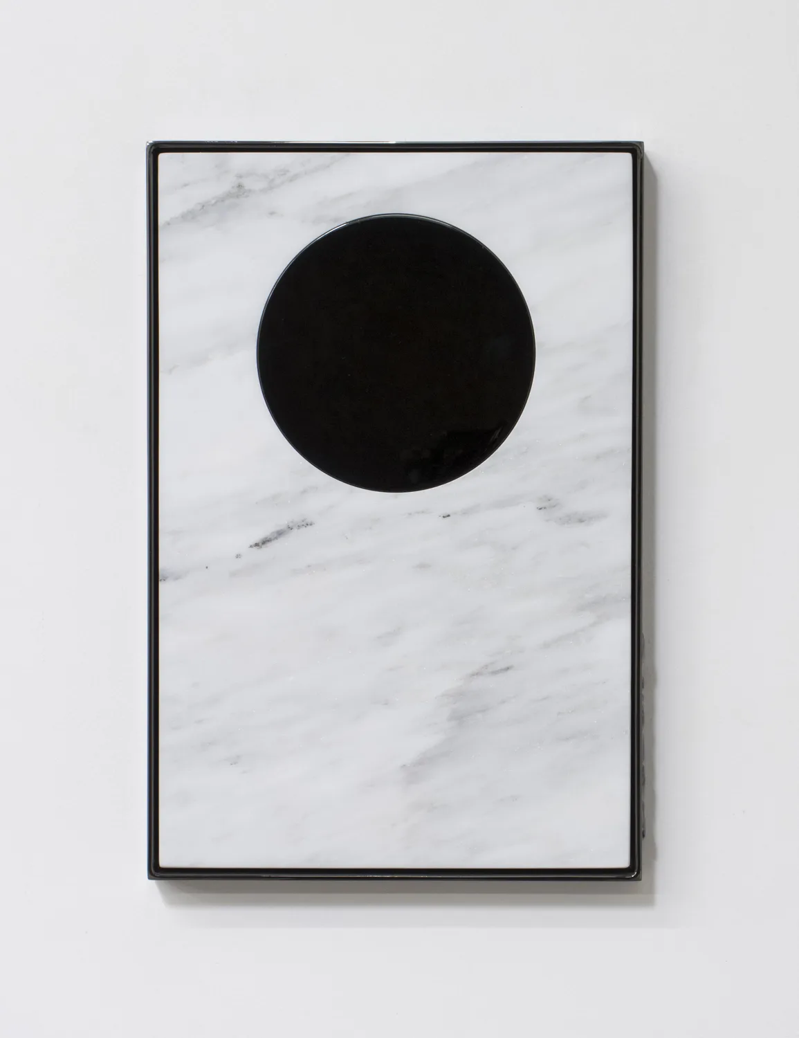 A small panel black chrome plated steel piece that has carrara marble that represents a perfect floating circle becomes reminiscent of the moon