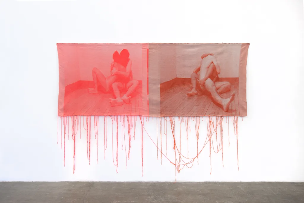 A pink and maroon woven tapestries depict photographic images of two nude individuals that is intimate