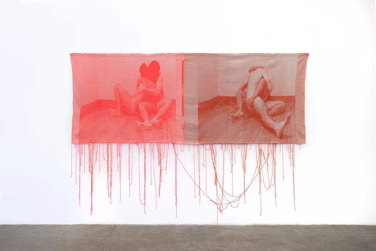 A pink and maroon woven tapestries depict photographic images of two nude individuals that is intimate