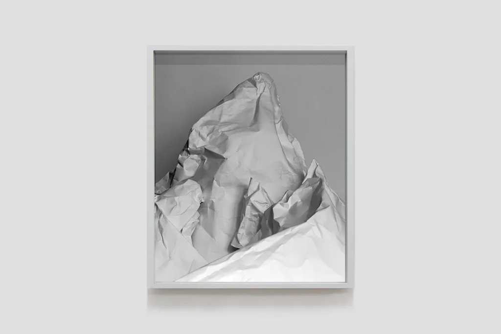 Installation image of Ohan Breiding's Playing Submarine show, of one portrait hanging on the wall. It shows a white crumbled paper shaped-like a mountain.