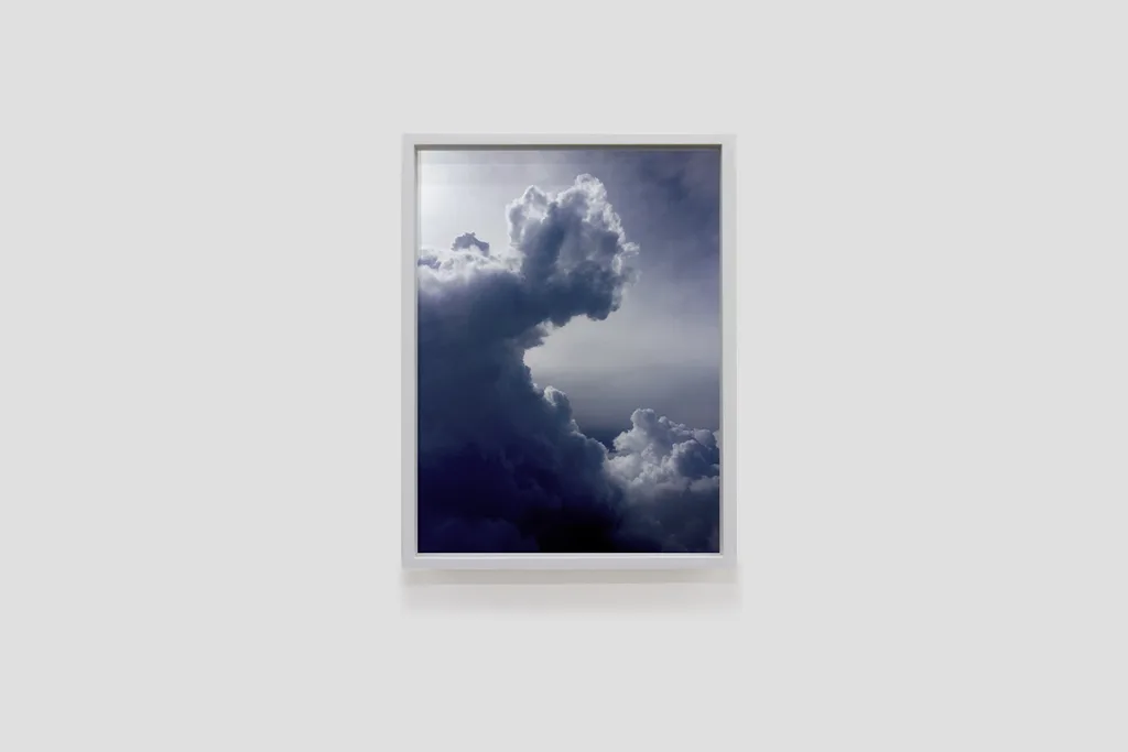 Installation image of Ohan Breiding's Playing Submarine show, of one portrait hanging on the wall. It shows a photo of a cumulonimbus clouds