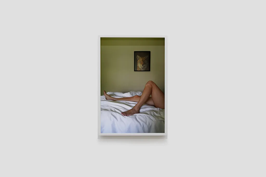 Installation image of Ohan Breiding's Playing Submarine show, of one portrait hanging on the wall. It shows a light-medium-skinned woman laying on the bed and showing her legs