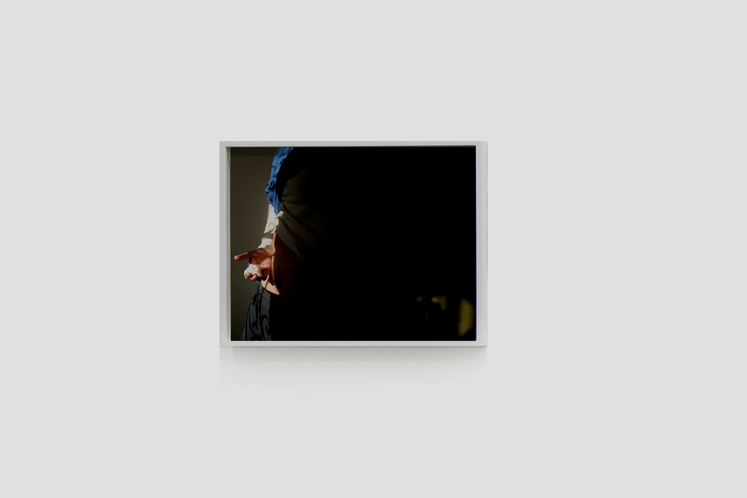 Installation image of Ohan Breiding's Playing Submarine show, of one portrait hanging on the wall. It shows a man is holding like a cottage cheese object with a right hand