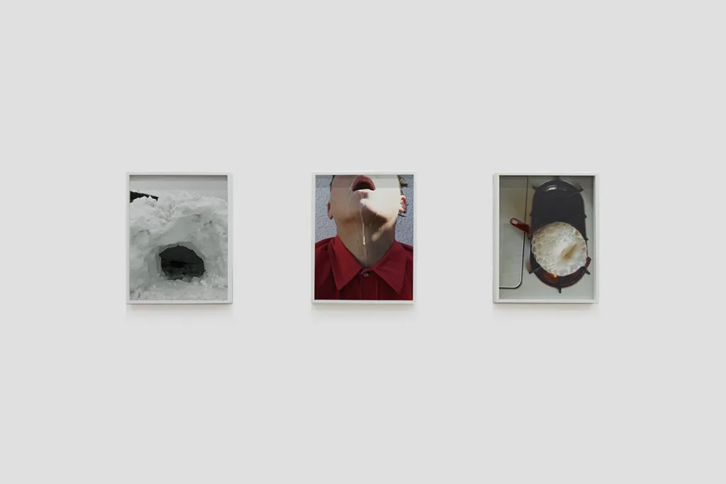Installation image of Ohan Breiding's Playing Submarine show, of about three portraits hanging on the wall. The first one is a concave image of a snow cave, the second one is a photo of a milk that is dripping out of a man's mouth. Last one is a boiling milk in a red pan