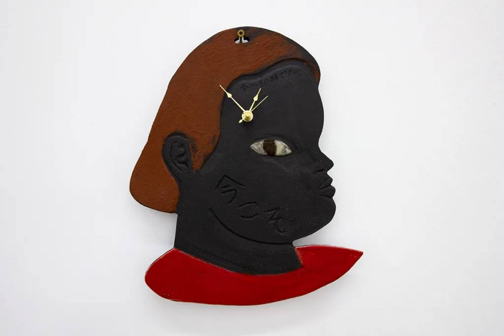 A black ceramic human figure is facing east. There are an hour, minute, and second clock hand in the right temple