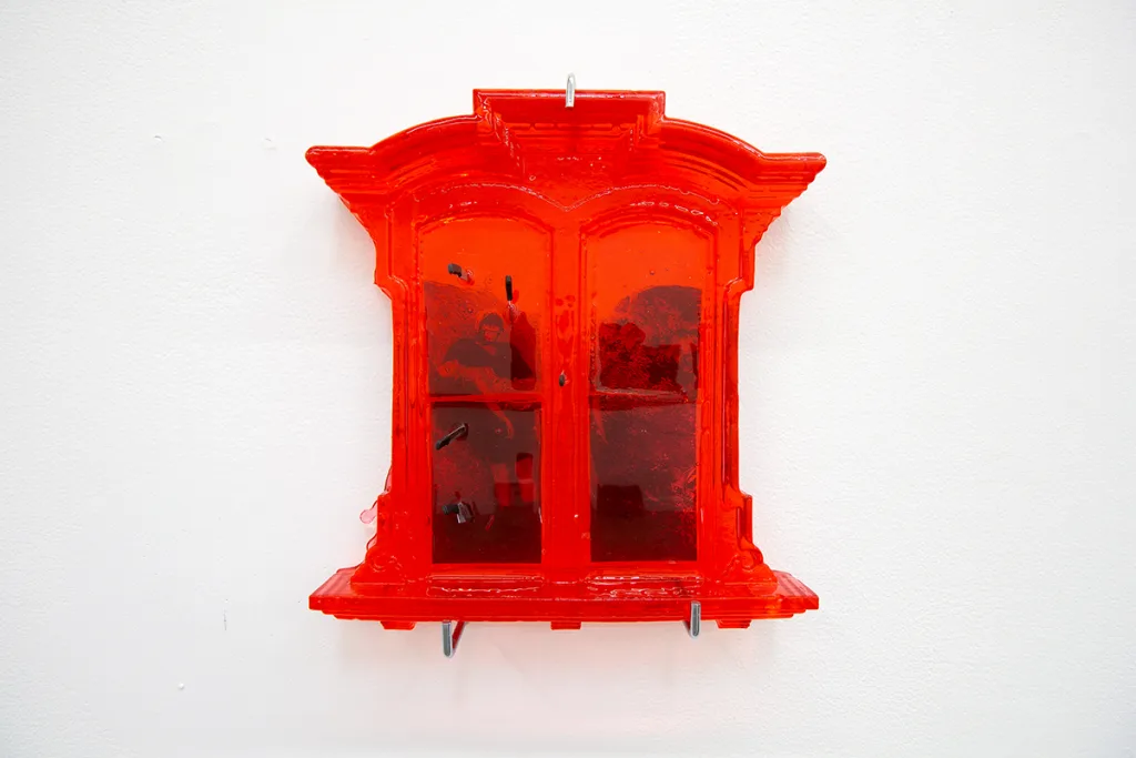 A red window and picture of a man carrying a lady in a bridal way that is attached on a glass of the window