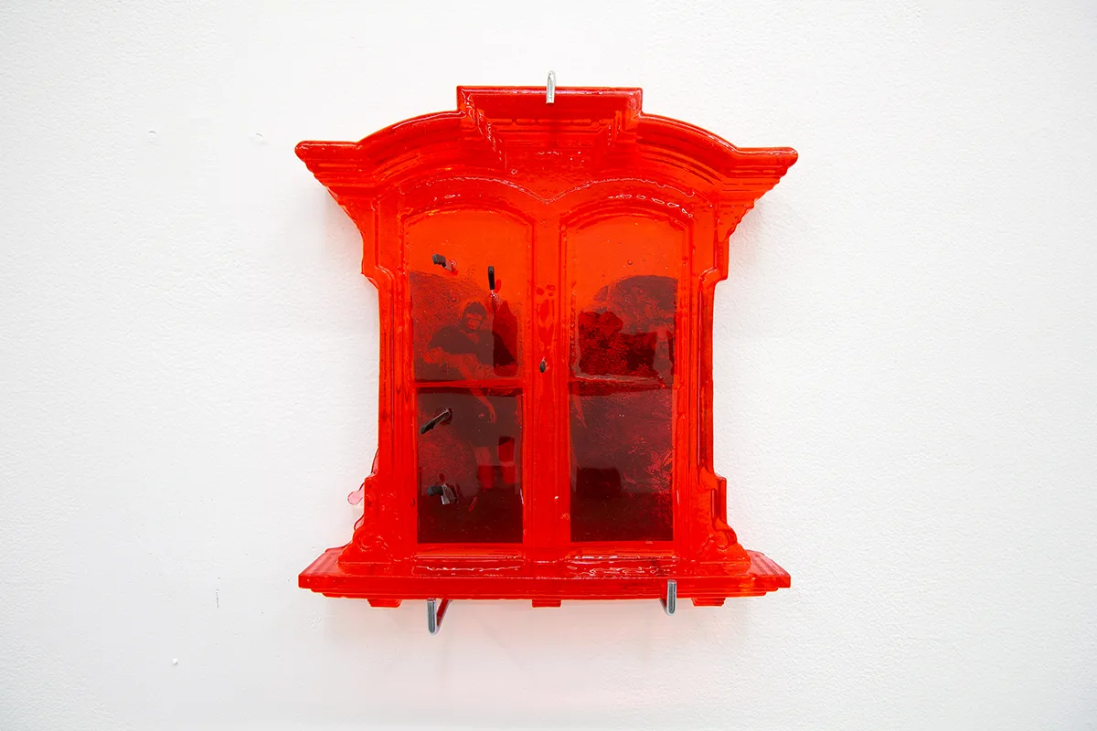 A red window and picture of a man carrying a lady in a bridal way that is attached on a glass of the window