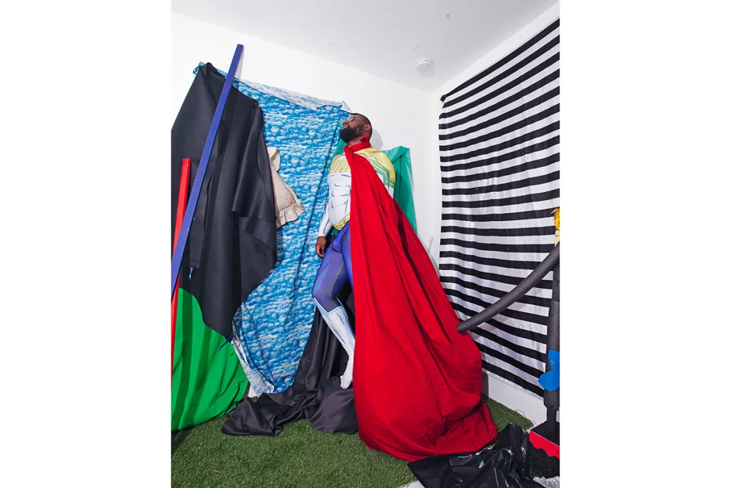 A dark skinned man is wearing a polyester superhero costume with red cape