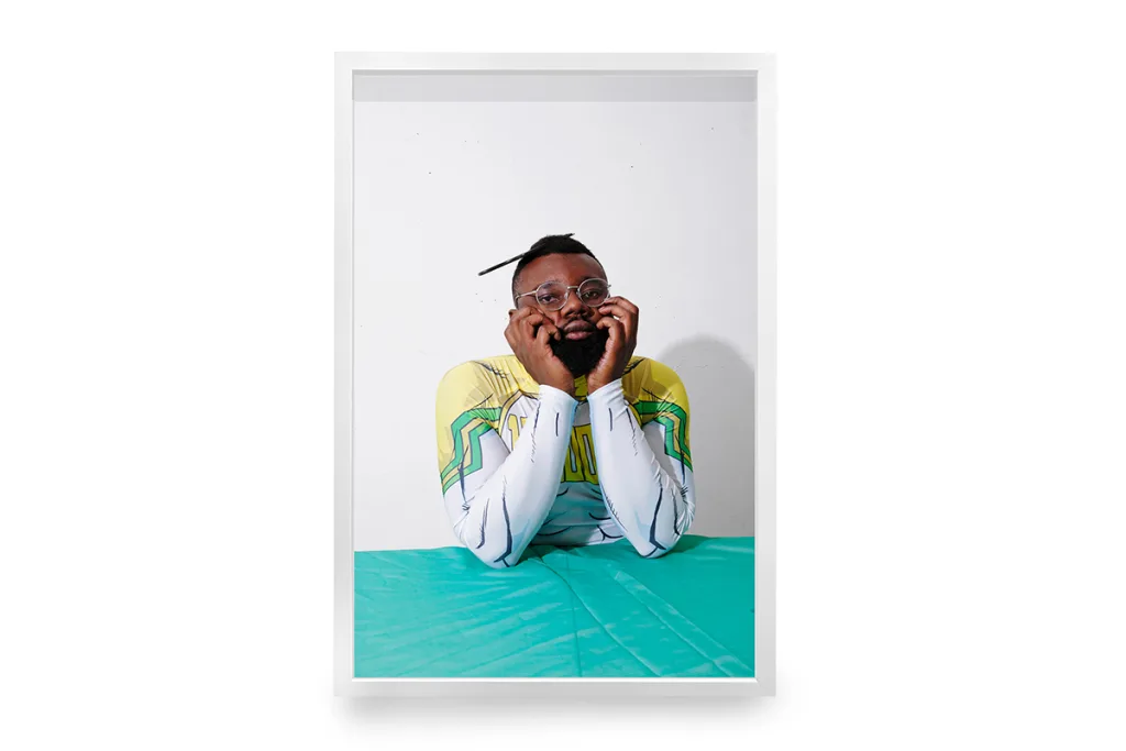 A portrait of a dark skinned man with his chin leaning on his both hands and staring intensely