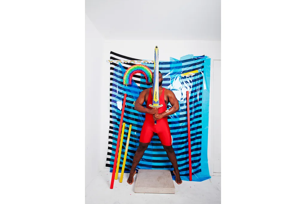 A dark skinned man wearing a red leotard and a oversized sword