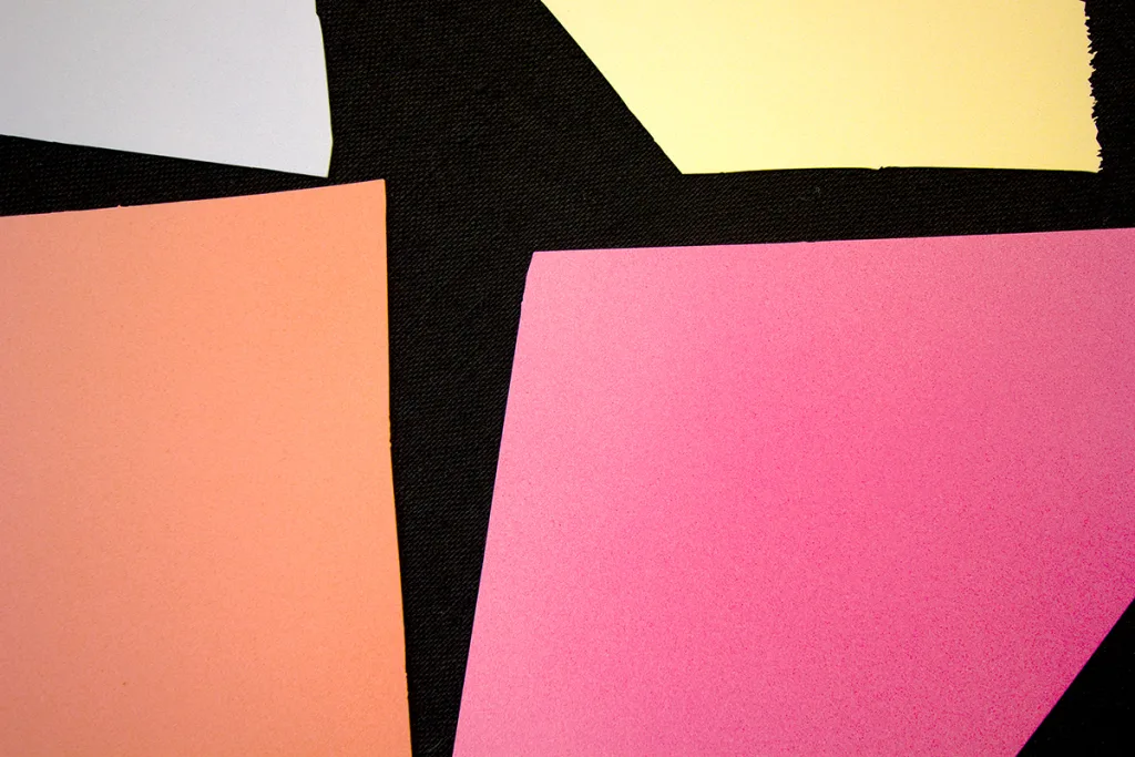 A detailed image of a work that features a black panel that has a multi colors of bright and vivid papers collage on the surface
