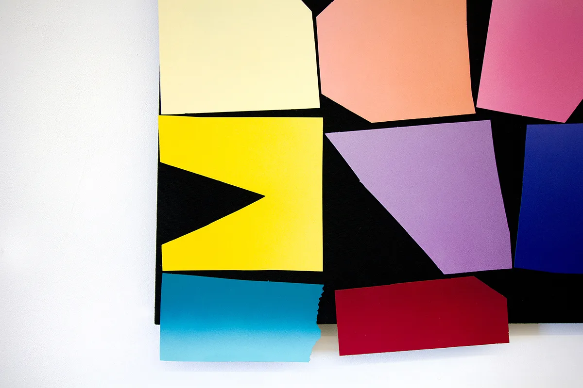 A detailed image of a work that features a black panel that has a multi colors of bright and vivid papers collage on the surface