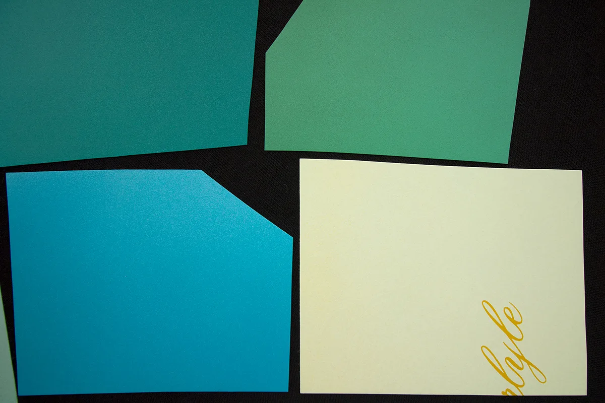 A detailed image of a work that features a black panel that has green papers collage on the surface