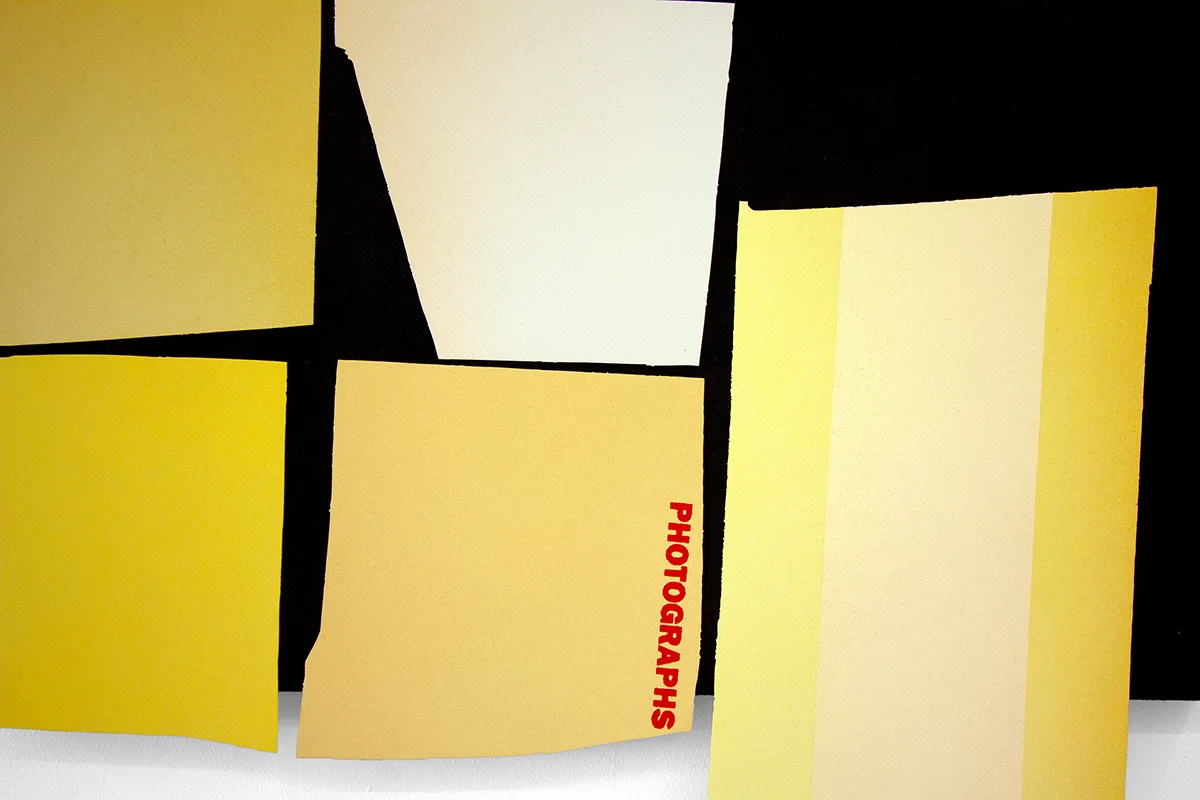 A detailed image of a work that features a black panel that has yellow papers collage on the surface