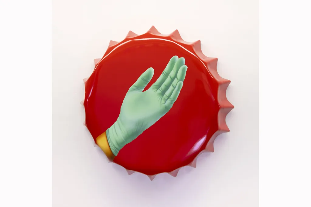 A metal cap-shaped painting shows a hand that is wearing a green gloves