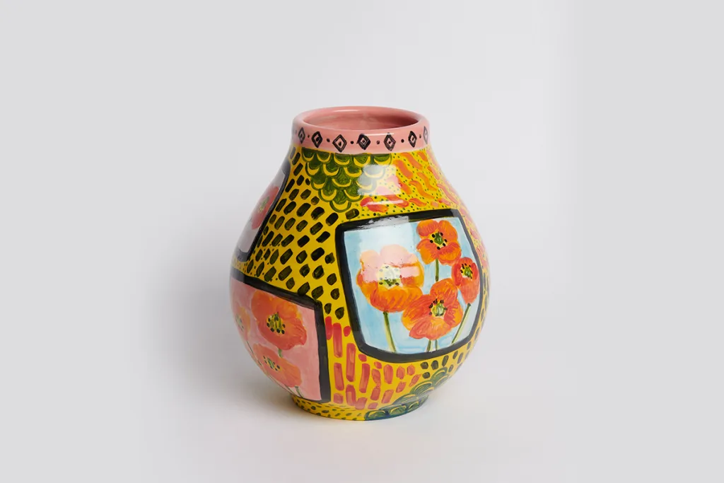 A sculpture by artist Anna Valdez of a yellow flower vase with poppies painted on it in different locations.