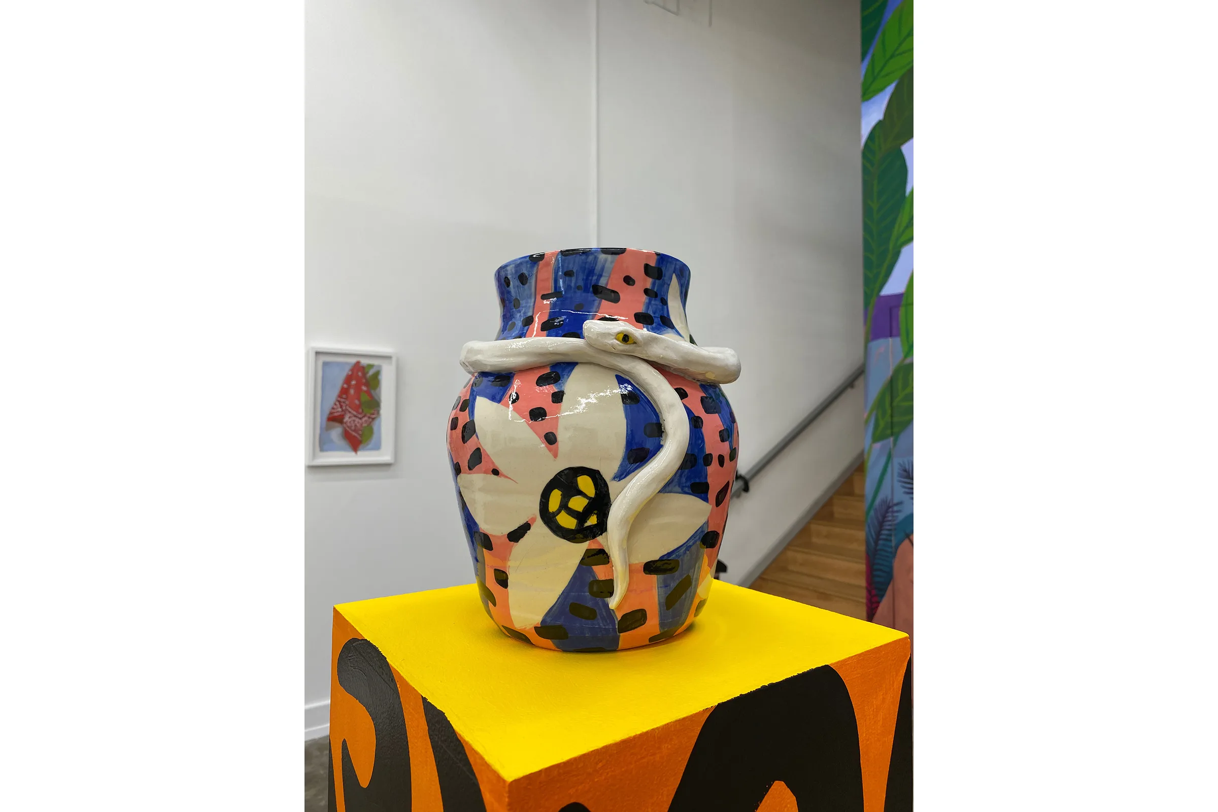 A painted ceramic vase by artist Anna Valdez with a flower painted on it, a snake coiling around the top of the vase.