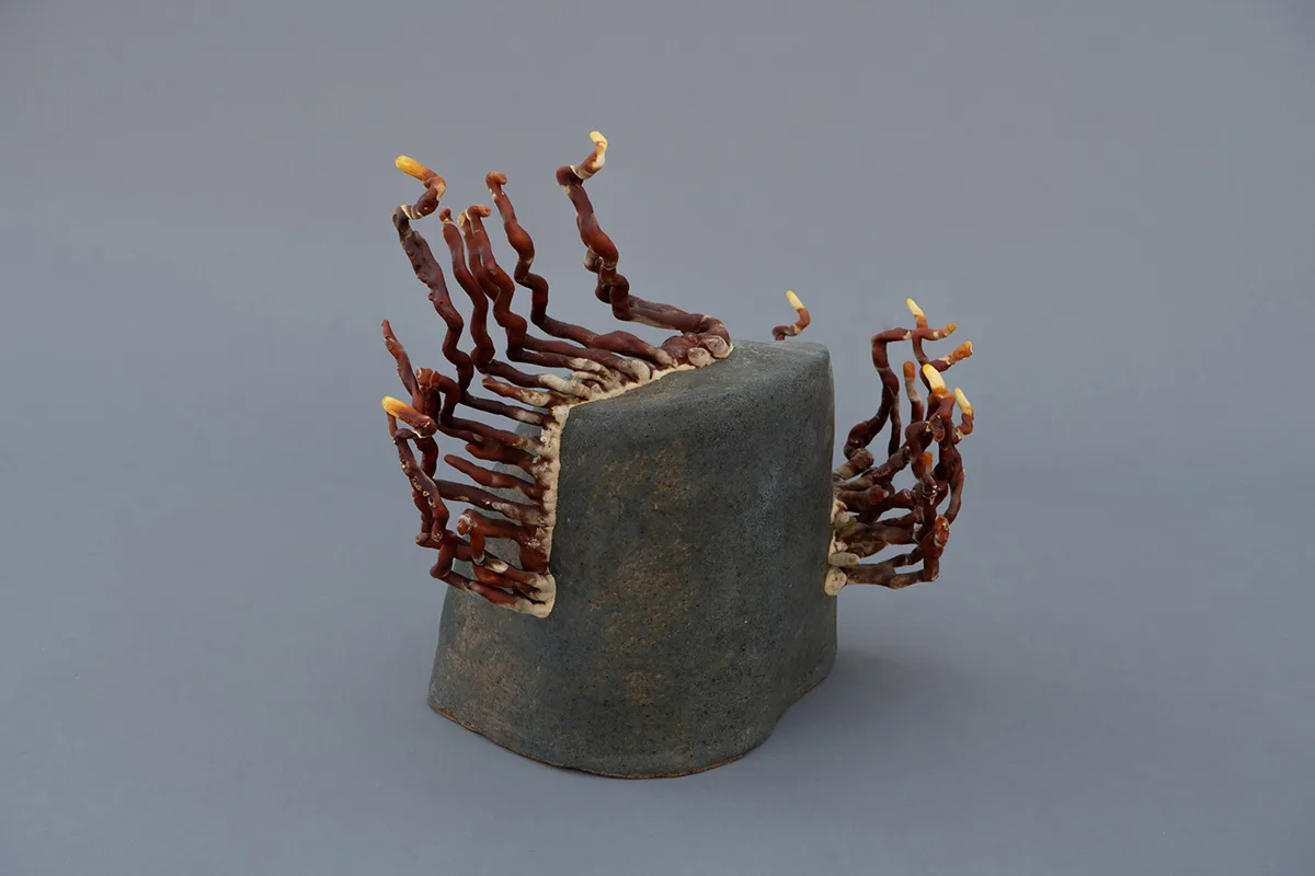 A sculpture by artist Sam Shoemaker of a stone shape with mushrooms growing off of it.