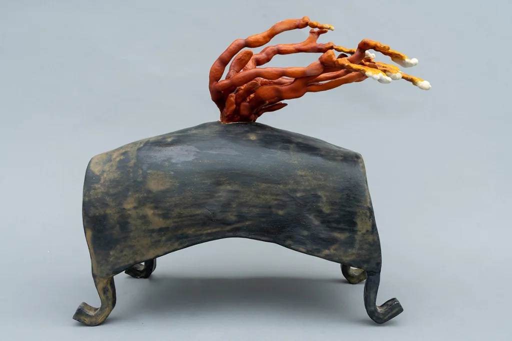 A sculpture by artist Sam Shoemaker of a stone shape with mushrooms growing off of it.