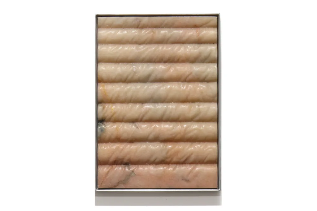 A carved marble sculpture by artist Devin Farrand depicting a puff jacket (pink marble).
