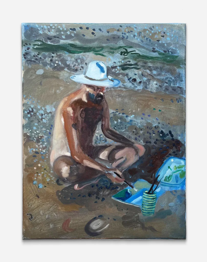 a figure sits on the beach in a white hat and paints.
