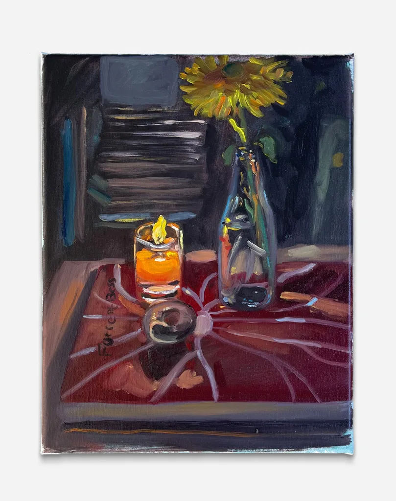 a book is used to sit a lit candle, sunflower in a vase, and an unidentifiable round object