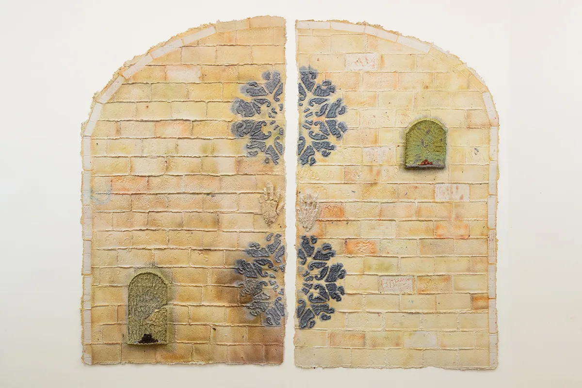 Two half-arches made of yellow tinted handmade dyed paper and embossed with bricks. Also contains two paper pulp hands, shelves, and patterns protruding from the surface.
