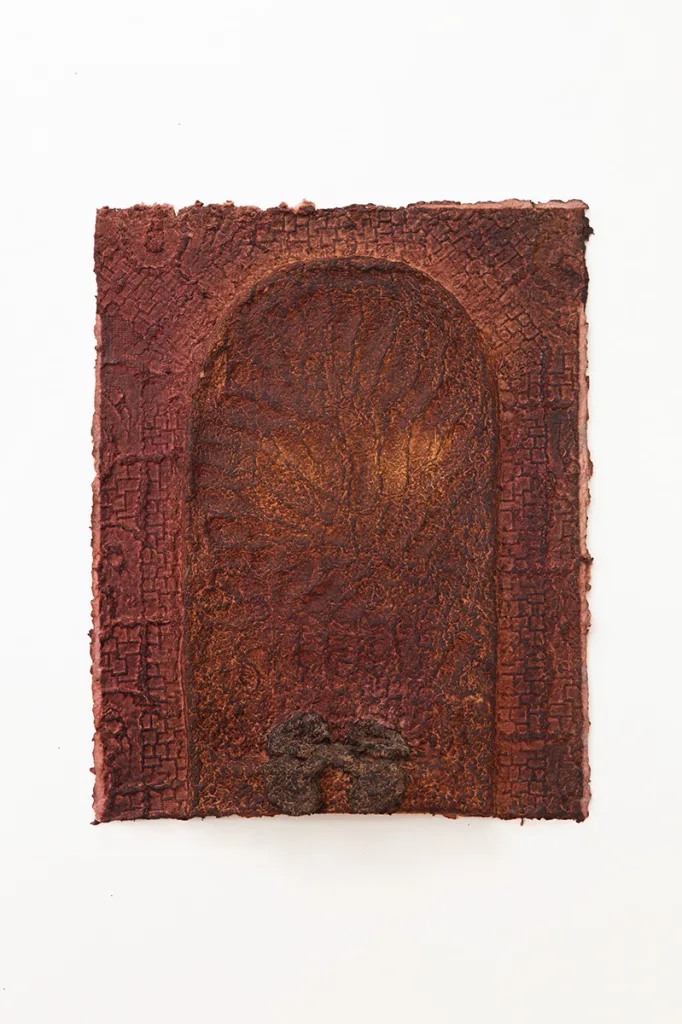 Red handmade dyed paper containing an archway, finger impressions, and a paper pulp flower.