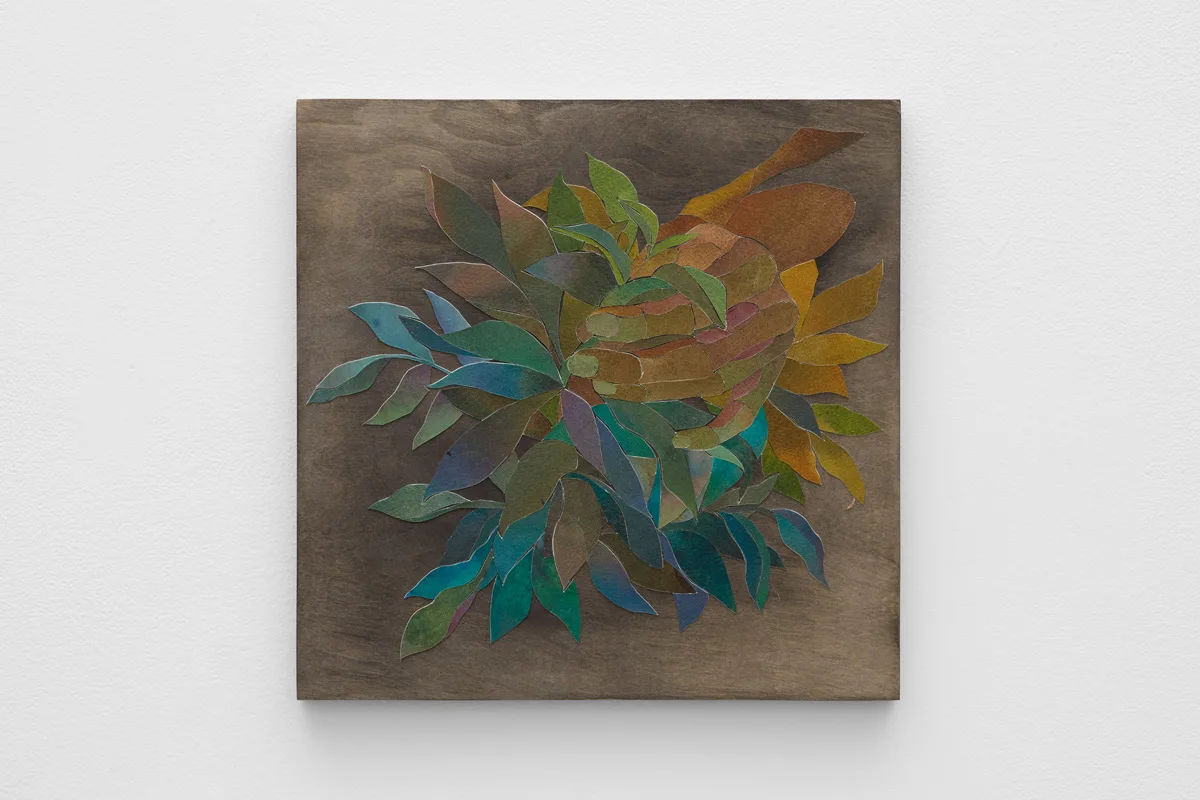 Ink on cut paper arranged to form a hand gripping an orange with a bunch of leaves surrounding. Mounted on a wood panel with a dark gray stain