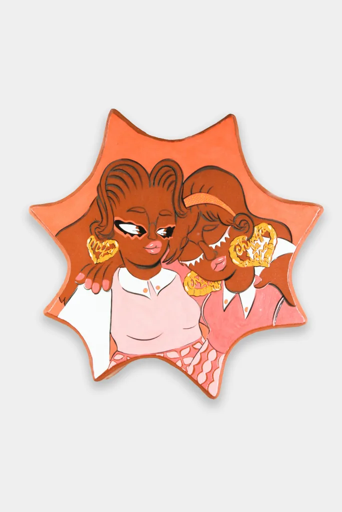 An amoeba shaped glazed ceramic wall-work depicting a two women holding each-other by the shoulders. The one on the left looks over at the other one in a supportive manner, while the one on the right tips her head down with closed eyes.