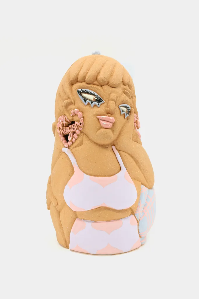 A carved and glazed ceramic vessel depicting a woman looking off to the side with earrings that read "Chingona."