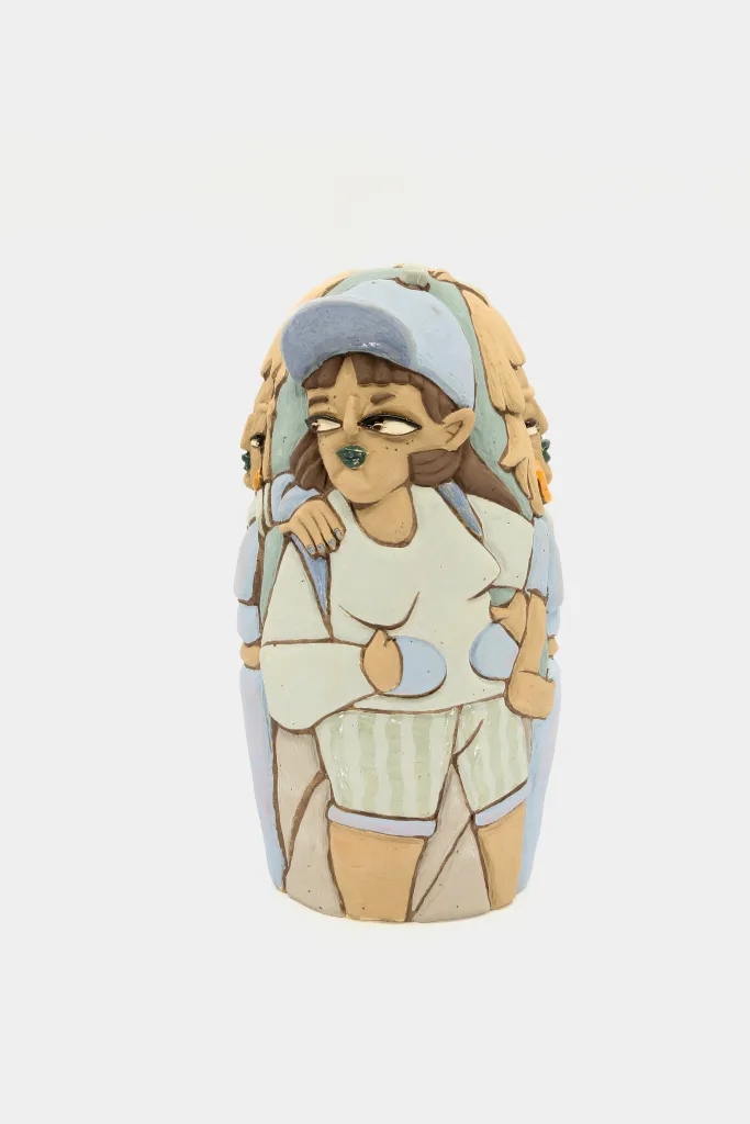 A carved and glazed ceramic vessel depicting a few women in motion. The one in the front has a blue cap on with a backpack. She looks off to her right with an empowering gaze and appears to be mid-stride.