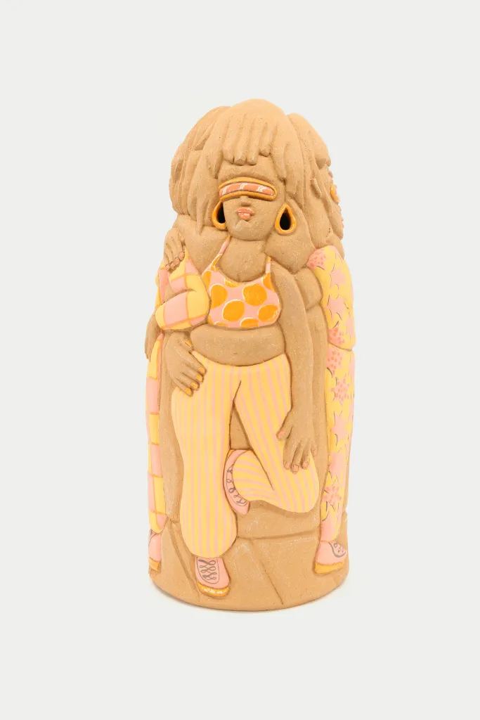 A carved and glazed ceramic vessel depicting a group of women wearing light orange outfits. The one in front looks up and holds her gaze confidently as the others stand by her side.