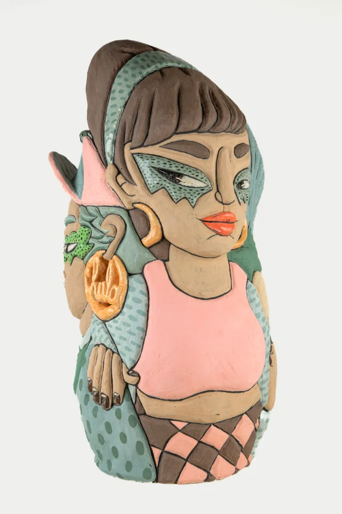 A carved and glazed ceramic vessel depicting two women leaning back to back. The one in front looks off to the side with a speculative gaze. The other's earring appears on the left side of the vase reading "Chula."