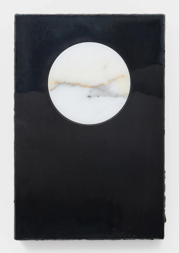 A circle cut from marble is nested within a plate of blued steel. The steel has sandblasted marks that extend the marble's natural lines past its edges and into the steel. They also resemble mountains in the distance.