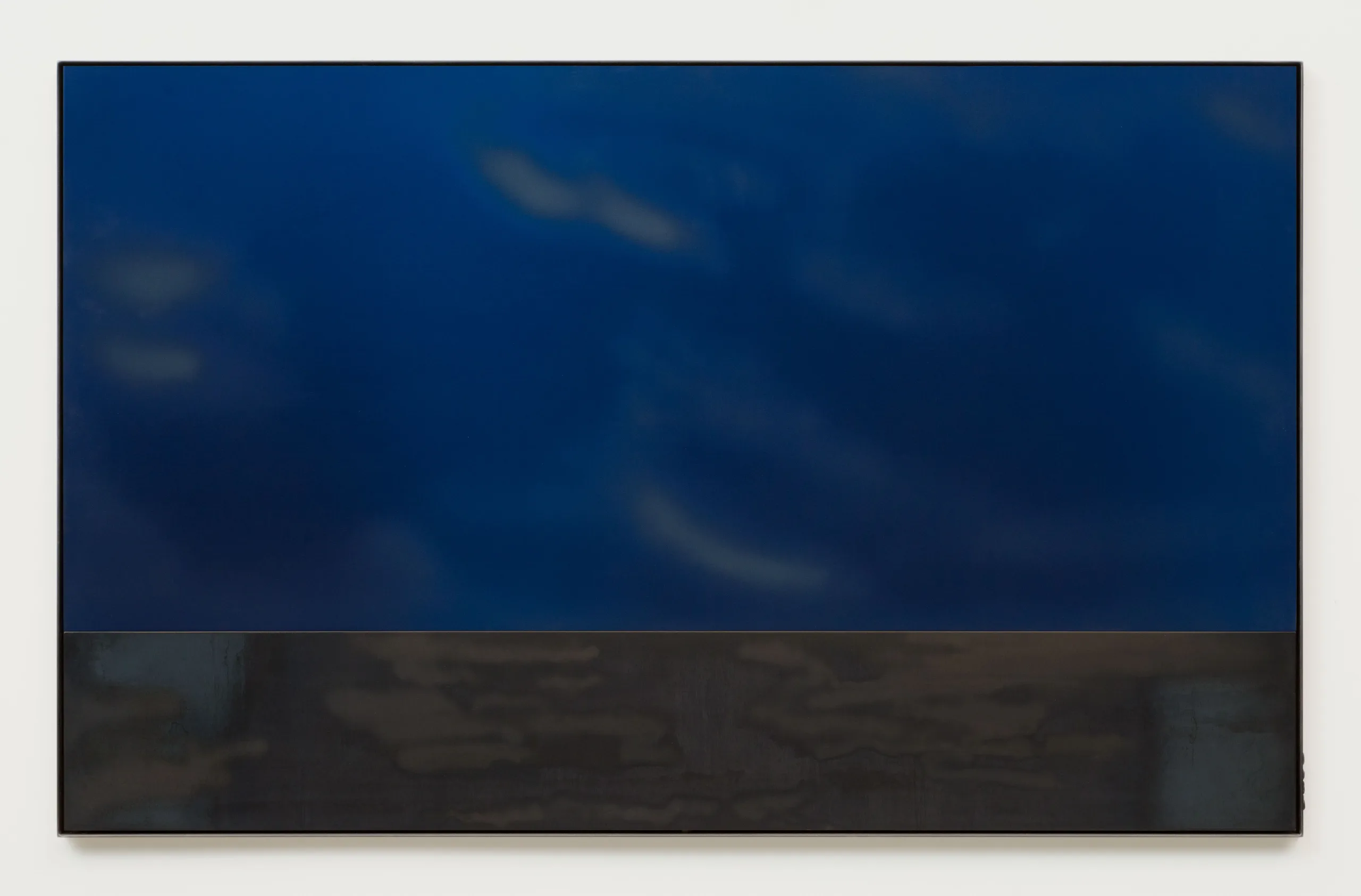 A deep blue plate of anodized aluminum with cloud-like sandblasting marks sits above a blued steel plate within a blued steel frame. The blued steel is a very dark grey color with a hint of blue, and is sandblasted with light horizontal marks.