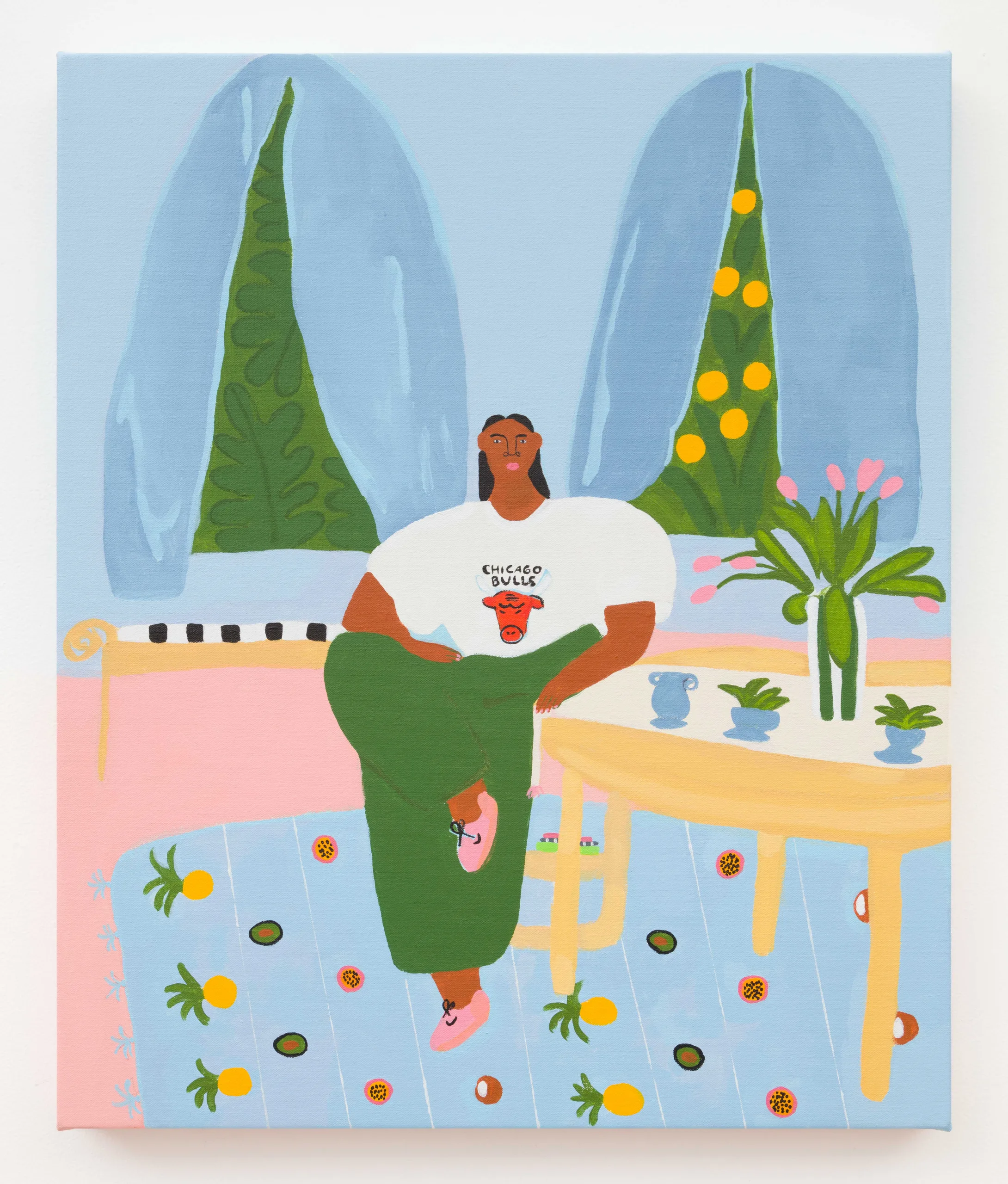 A painting of a woman sitting at a table, facing the viewer, wearing a chicago bulls t-shirt. Through the blue drapes behind her we see lush green foliage and below her is a rug with a fruit pattern decoration.