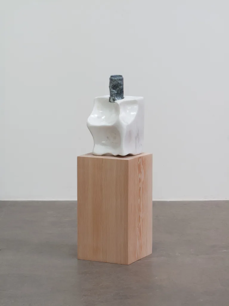 A carved marble sculpture resembling a salt lick and a carved soapstone beer can sit atop a wood pedestal.